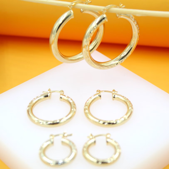 Three pairs of graduated gold hoop earrings hang and display on a white stand against an orange background.