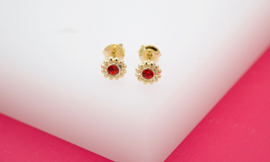 A pair of gold flower-shaped stud earrings featuring vibrant red crystals rests on a white display surface.