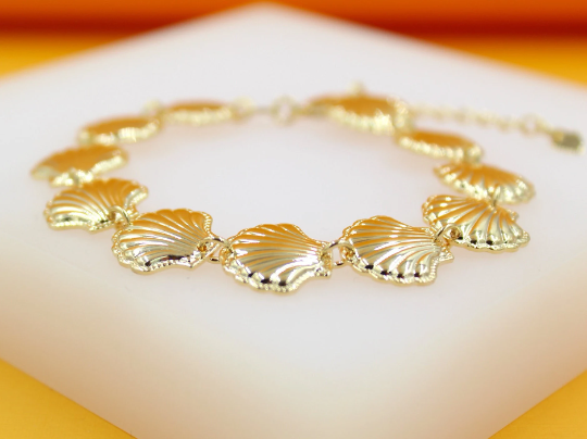 A gold seashell charm bracelet rests on a white display stand.