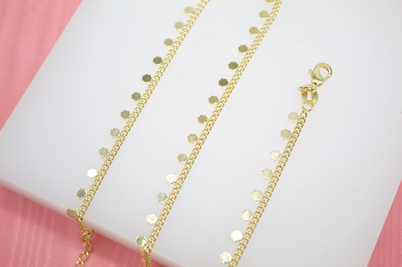 A delicate gold chain bracelet features hanging hexagonal coin charms displayed on a white surface.