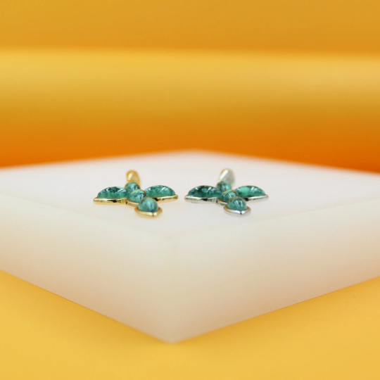 Two gold-plated butterfly charms with green gemstone accents rest side-by-side on a white display surface against a warm yellow background.