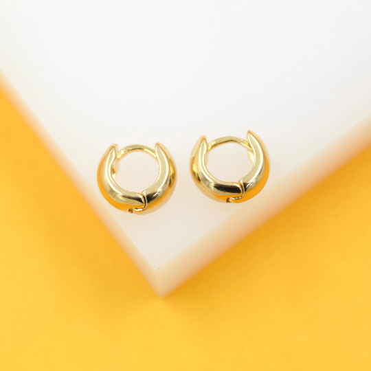 A pair of polished gold huggie hoop earrings rests elegantly on a clean white and yellow display block.
