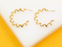 Two gold spiral hoop earrings rest on a white surface against a bright yellow background.