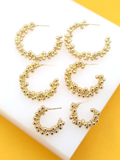 Three pairs of textured gold bead hoop earrings are displayed in descending sizes on a white platform.