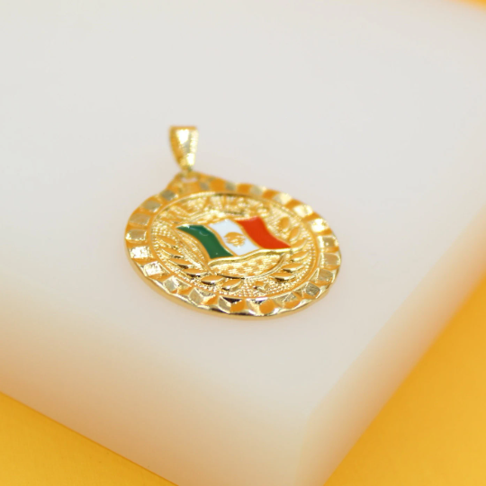 A gleaming gold pendant features an enameled Mexican flag design resting on a white display surface.