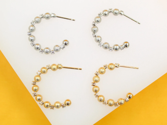 Two pairs of beaded hoop earrings, one in silver and one in gold, rest side by side against a white and yellow background.