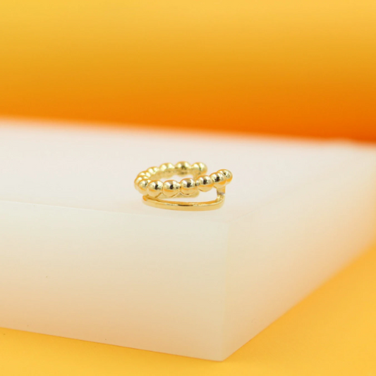 A gold double-band ear cuff featuring a beaded texture rests on a white display block.