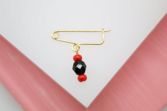 A gold safety pin brooch features a dangling charm made of a faceted black bead flanked by two small red beads.
