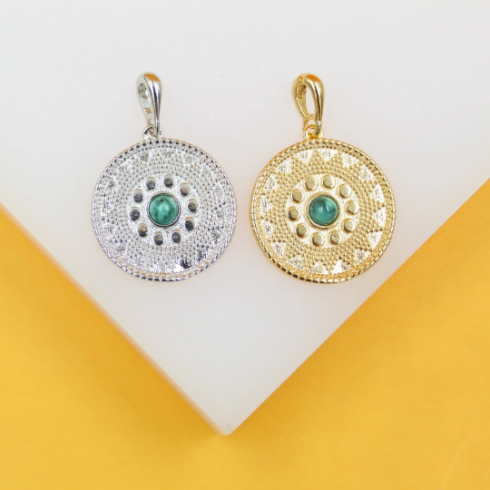 Two round, textured metal pendants featuring green center stones rest on a white display stand.