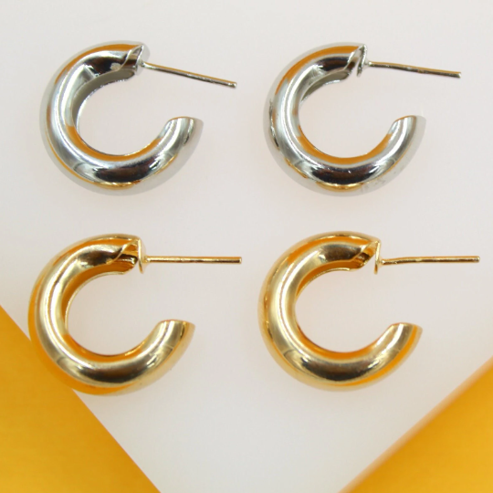 Four chunky hoop earrings, two silver and two gold, rest neatly on a white and yellow display surface.