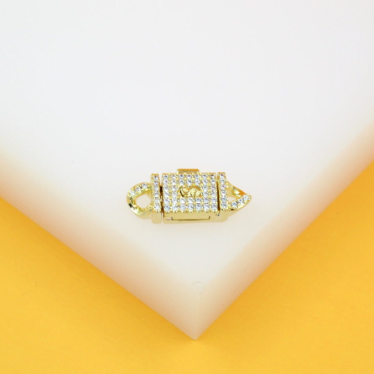 A gold padlock-shaped charm sparkles with pavé stones against a white and yellow background.