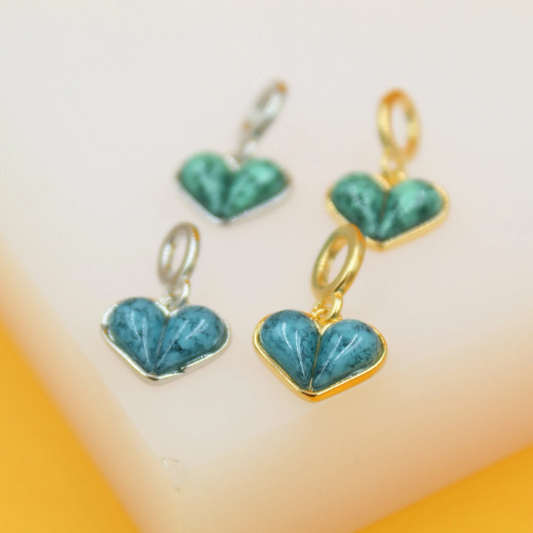 Four turquoise heart-shaped charms rest on a light surface, showcasing gold and silver settings.