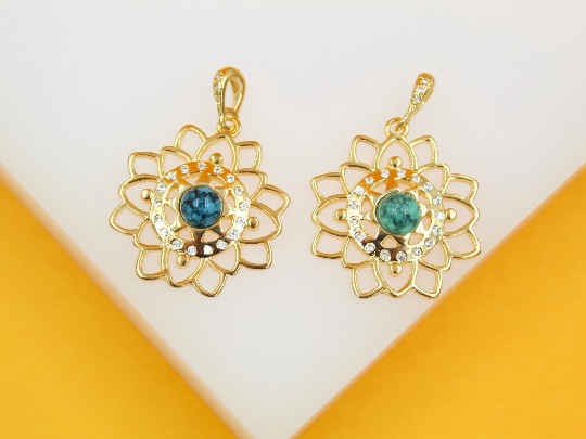 Two gold lotus flower pendants featuring central turquoise stones and sparkling cubic zirconia accents rest against a bright white and yellow background.