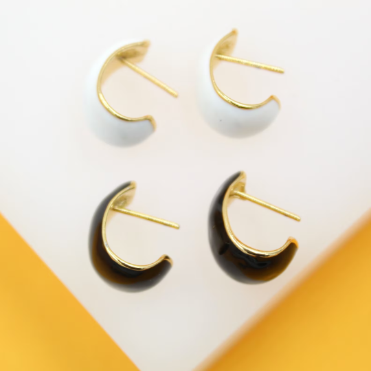 Four half-hoop earrings featuring gold rims and glossy enamel in black and white display on a white surface.