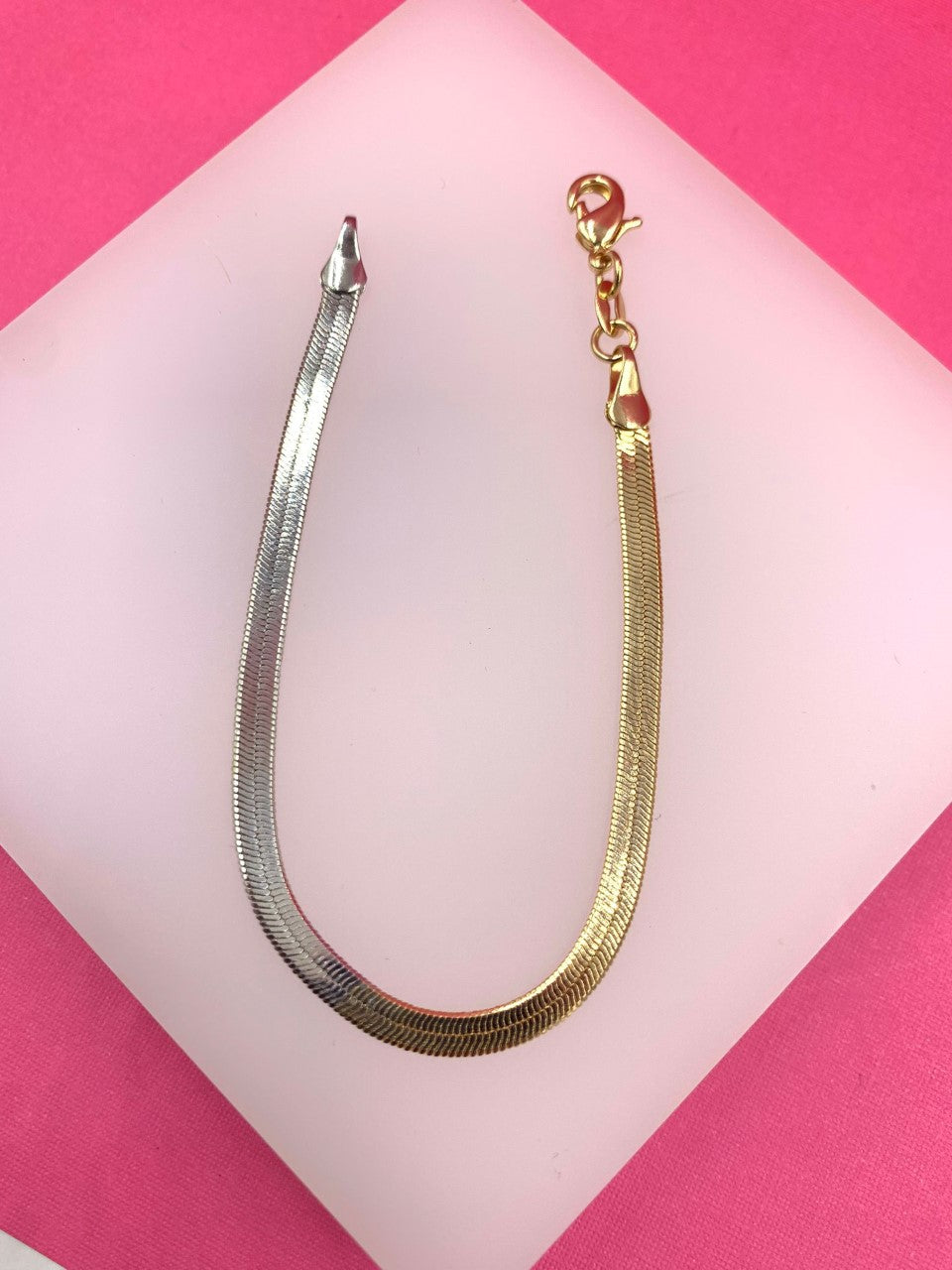 A two-toned herringbone chain bracelet rests gracefully on a pink surface.