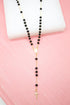 A delicate gold rosary necklace featuring glossy black beads and a small crucifix rests against a soft pink and white background.