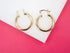 Two polished thick gold hoop earrings rest against a white surface set against a vibrant pink background.