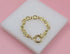 A gleaming gold anchor chain bracelet rests gracefully on a white display block against a soft pink background.