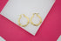 A pair of textured gold hoop earrings rests against a white display block over a vibrant pink background.