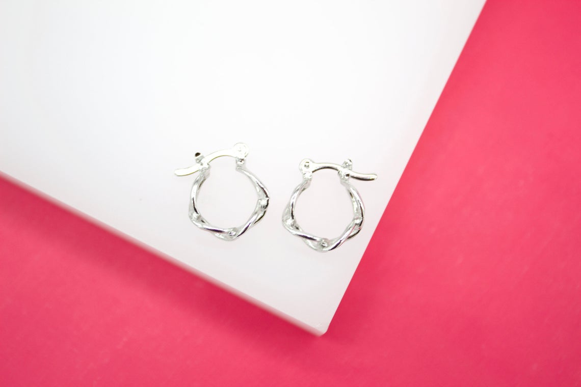 Two silver twisted hoop earrings rest on a white surface against a bright pink background.
