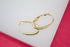 A pair of elegant gold hoop earrings with sparkling crystal accents rests on a white display surface against a pink background.