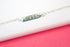 A delicate sterling silver ID bracelet rests on a white and pink display surface, showcasing an engraved floral pattern on its rectangular bar.