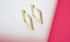 A pair of gold square huggie hoop earrings featuring sparkling pave-set stones display on a white display against a vibrant pink background.