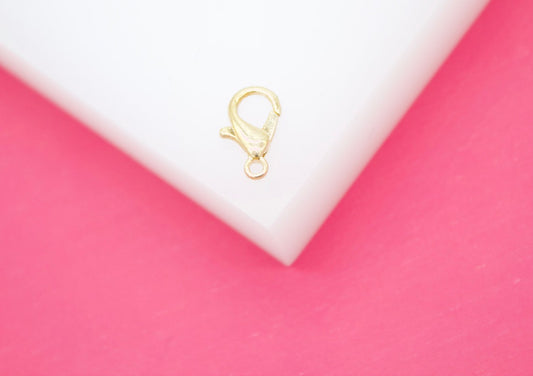 A small gold lobster clasp sits on a white surface against a bright pink background.