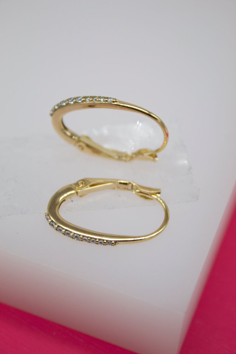 A pair of gold huggie hoop earrings featuring sparkling pave-set diamonds rests on a white display block.