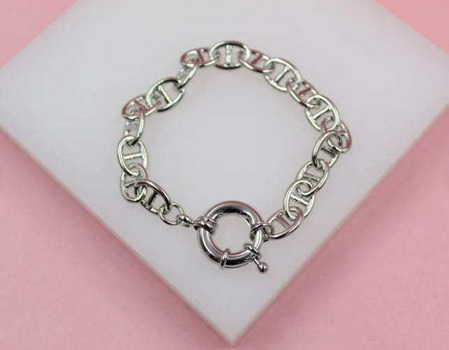 A polished silver Mariner link bracelet with a round spring ring clasp rests on a white display pad against a pink background.