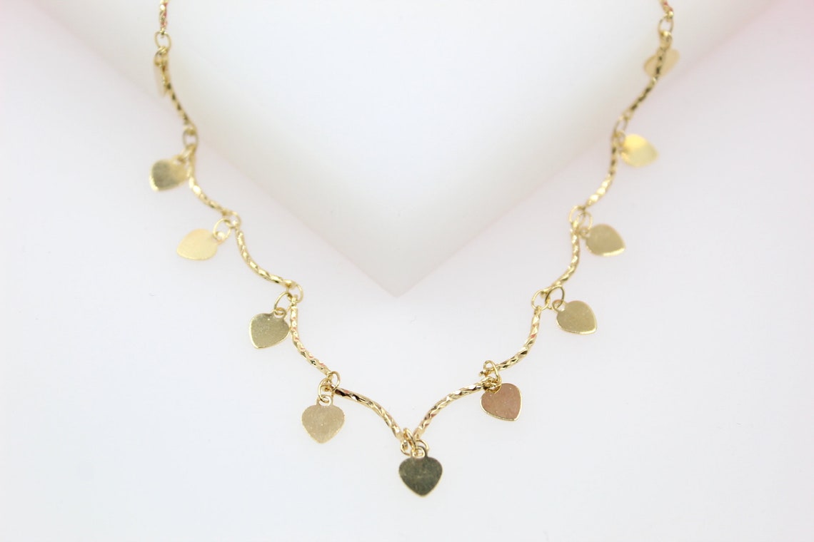 A delicate gold charm necklace features hanging heart-shaped pendants against a clean white background.