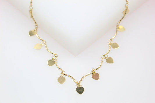 A delicate gold charm necklace features hanging heart-shaped pendants against a clean white background.