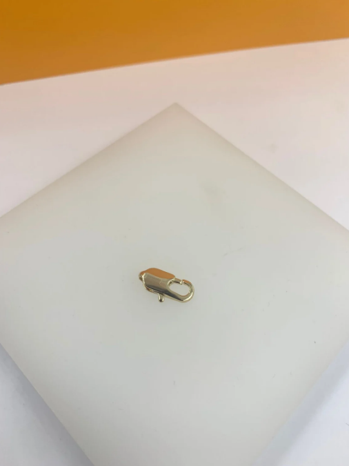 A small gold lobster clasp rests centered on a white display surface.