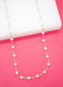 A delicate gold chain necklace with evenly spaced white pearls drapes gracefully over a white surface against a vibrant pink background.