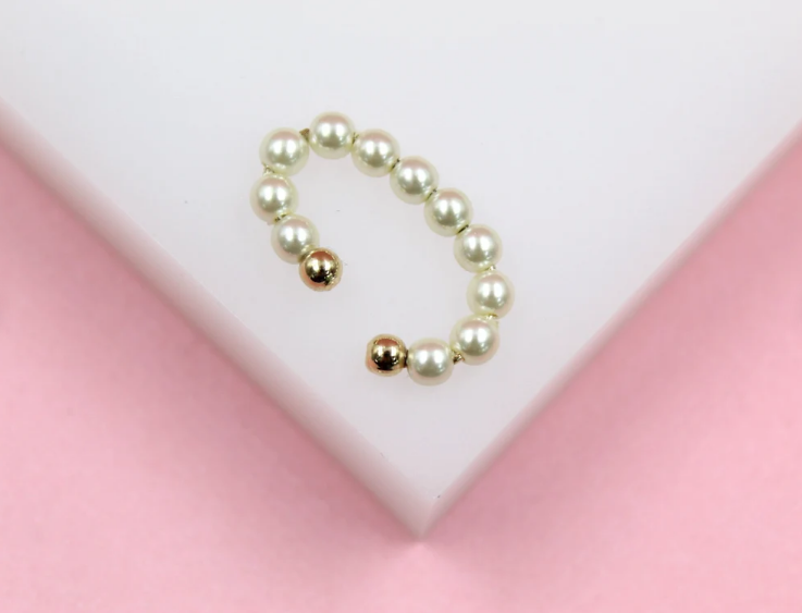 A delicate pearl ear cuff featuring alternating white pearls and gold beads rests on a white and pink surface.