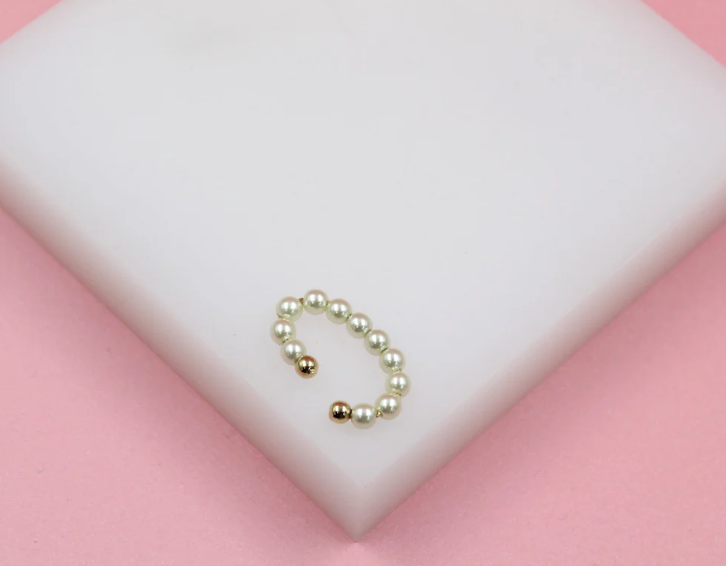 A gold pearl ear cuff rests on a white display surface against a pink background.