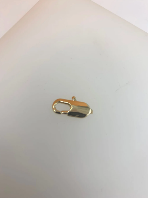 A shiny gold lobster claw clasp rests on a plain white surface.