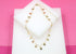 A delicate gold heart-charm necklace rests on a white display block against a vibrant pink background.