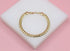 A shiny gold curb chain bracelet rests elegantly on a white display block against a soft pink background.