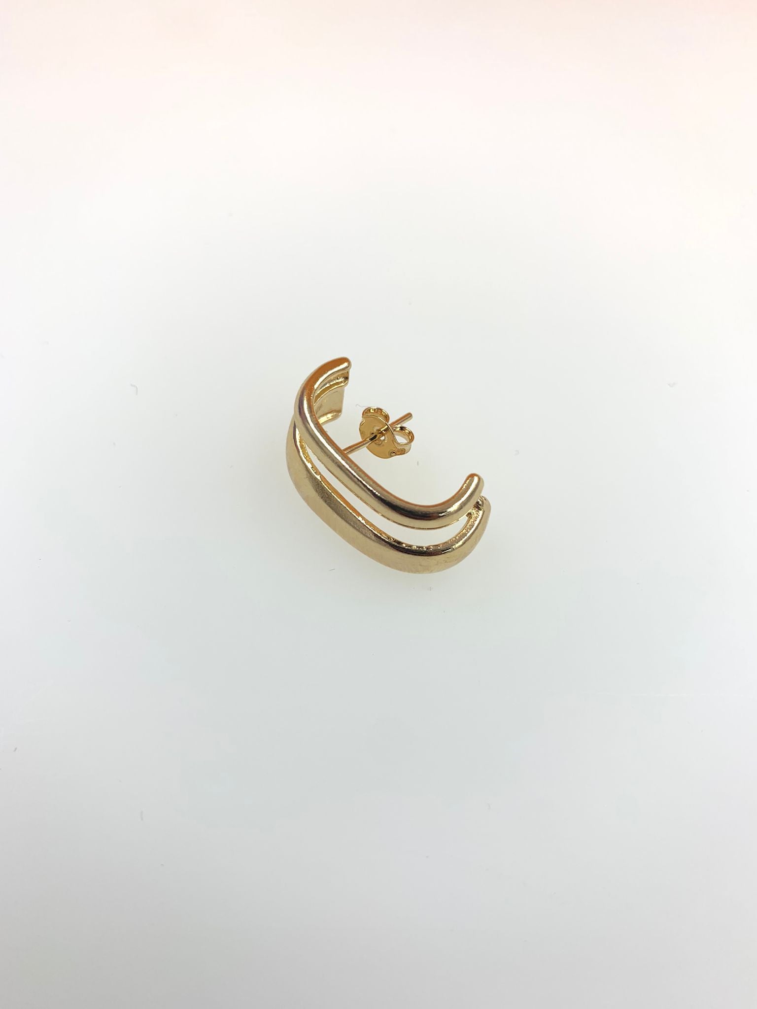 A sleek double-band gold earring rests against a clean white background.