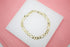 A delicate gold-filled Figaro chain bracelet rests gracefully on a white display against a pink background.