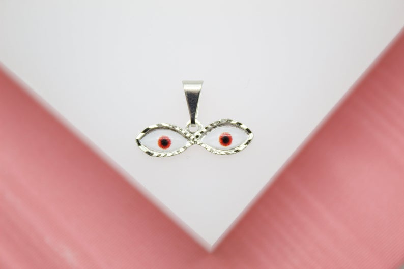 A silver evil eye pendant features two interconnected eye charms with red irises against a white enamel background.