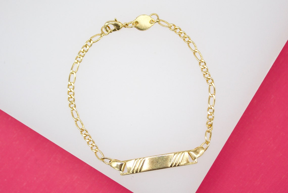 A delicate gold ID bracelet rests on a white and pink background.