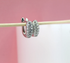 A pair of sparkling silver huggie hoop earrings encrusted with cubic zirconia stones hangs delicately on a wooden stick against a soft pink background.