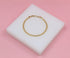 A delicate gold chain bracelet rests centered on a white display block against a soft pink background.