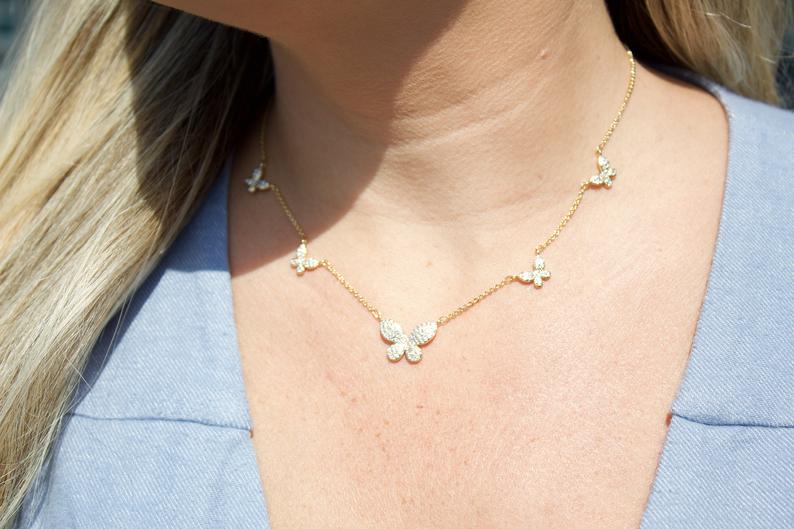A blonde woman wears a delicate gold butterfly pendant necklace featuring multiple sparkling diamond-encrusted butterflies along the chain.