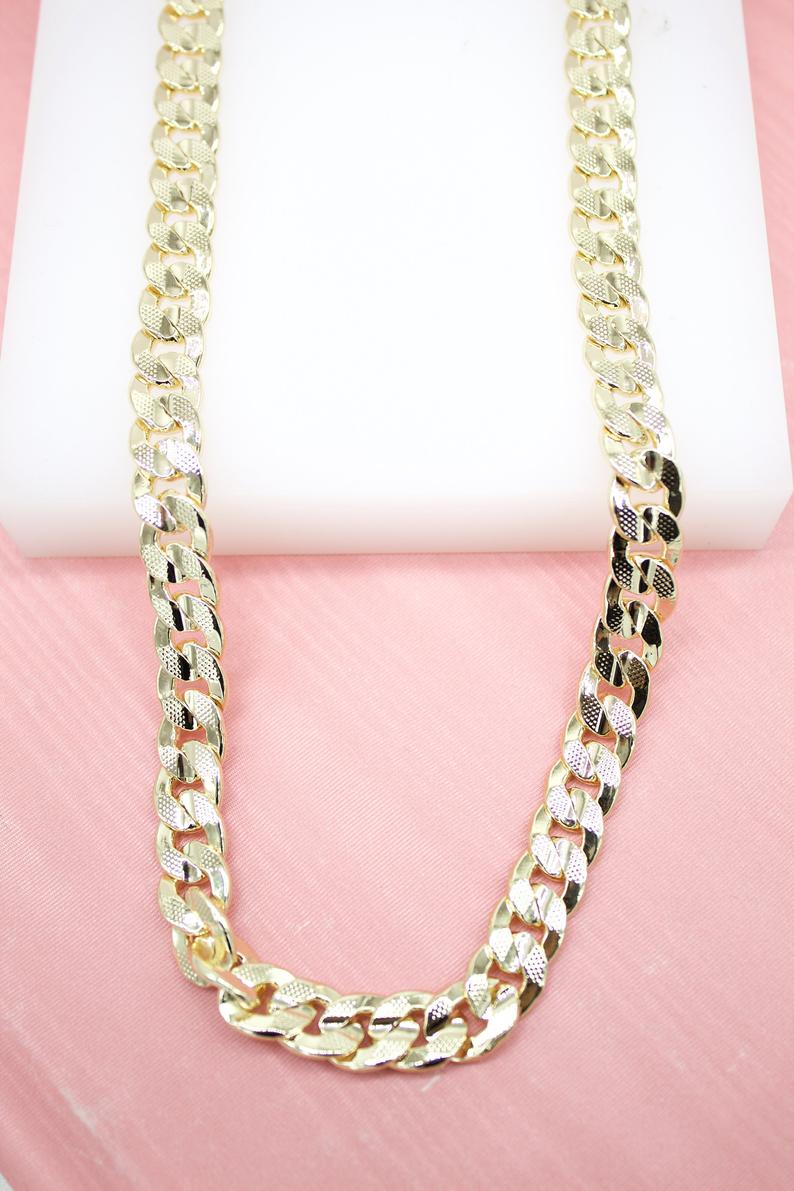 A thick gold-plated cuban link chain lies on a white display block against a pink background.