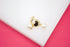 A pair of delicate gold heart-shaped earrings features dangling white pearls against a white and pink background.