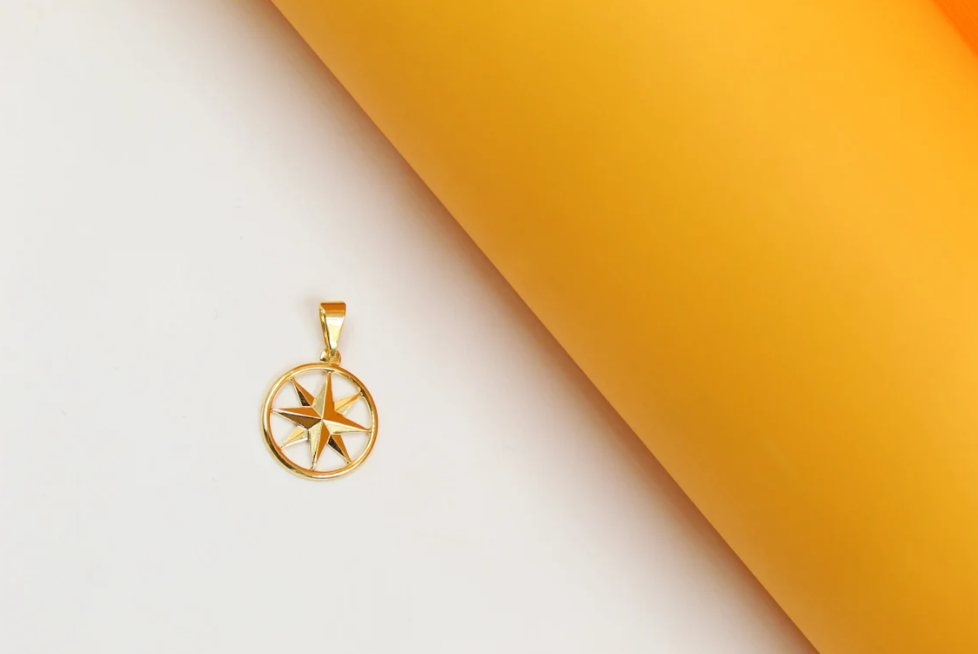 A polished gold compass pendant rests against a white and yellow background.