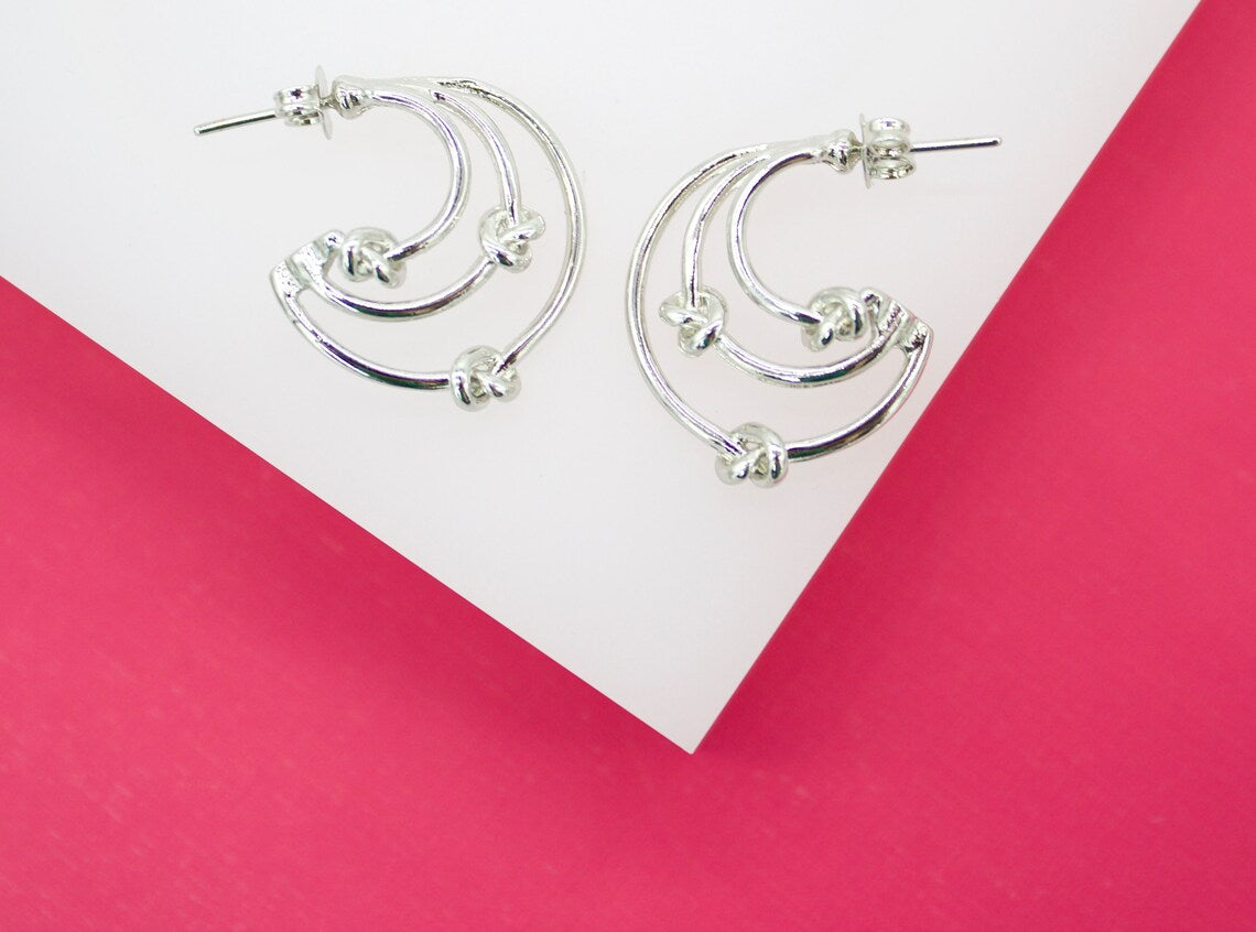 A pair of silver hoop earrings rests on a white and bright pink display surface.